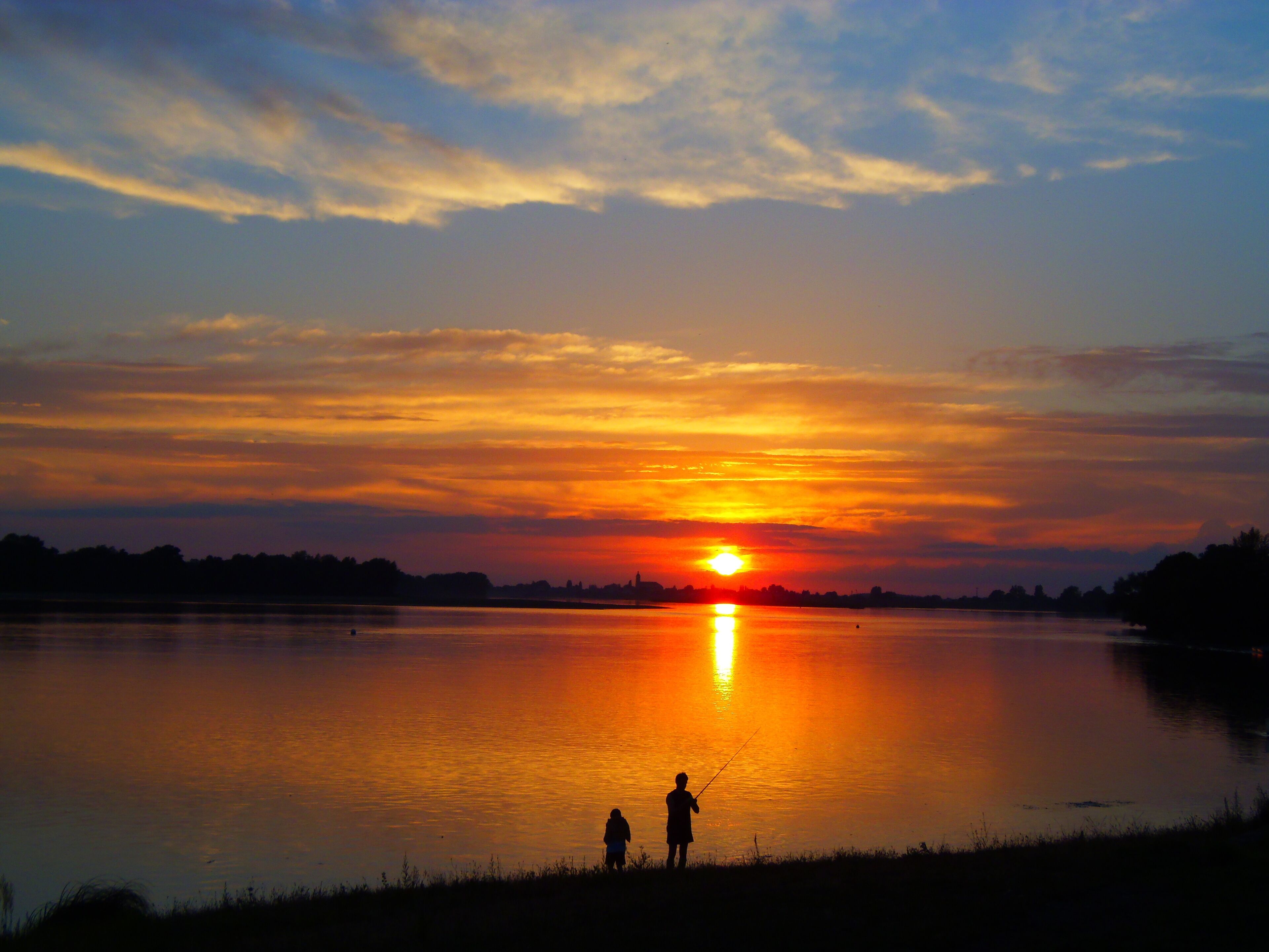 Un tramonto su un lago calmo con le sagome di due persone che pescano.