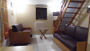 A compact living space with a sofa, a small table, a radiator, and a window with blinds. - A 10 kms d'ANGERS small independant house 2 persons quiet countryside (Loire-Authion)
