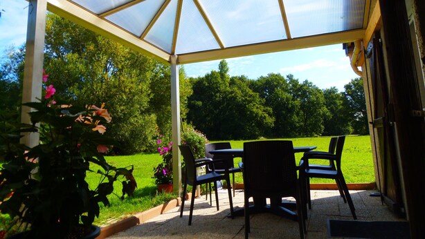 A covered patio area with a table and chairs, surrounded by potted plants and a view of a grassy field. - A 10 kms d'ANGERS small independant house 2 persons quiet countryside (Loire-Authion)