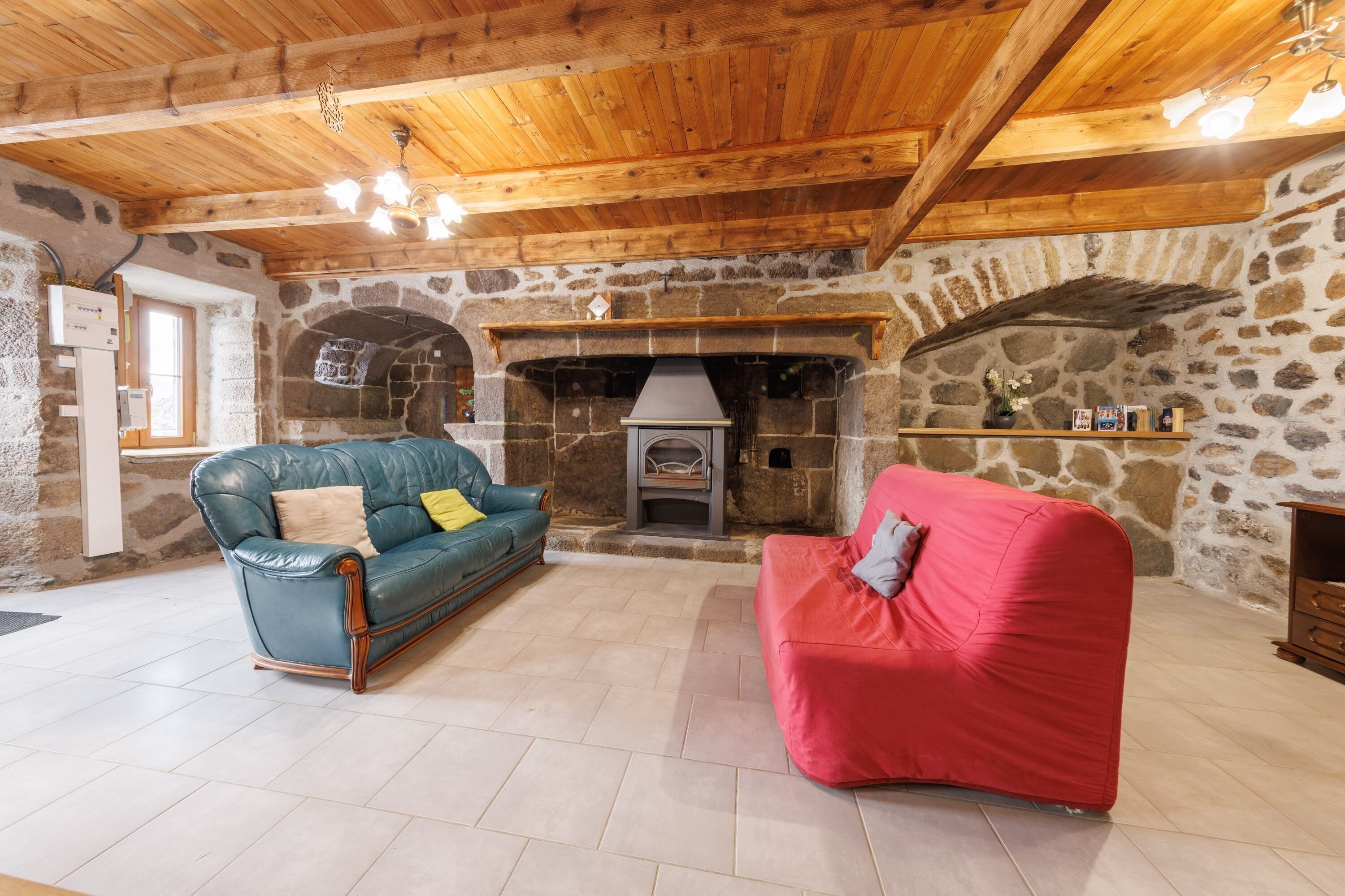 A cozy room with a stone fireplace, wooden ceiling beams, a blue leather sofa, and a red sofa.