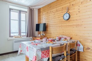 A cozy dining area with a wooden wall, a clock, and a table set for a meal. - Le Régit - Proche Station de Ski (La Bresse)
