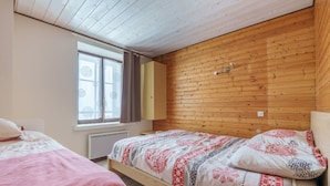 Makuuhuone, jossa on puinen katto, ikkuna, jossa on verhot, kuviollinen vuodevaatteilla varustettu sänky ja yöpöytä.