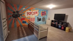 A room with a colorful wall mural, a bed, a TV, and a small cabinet.
