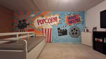 A room with a bed, a wall mural with movie and popcorn themes, a projector, and a clapperboard.