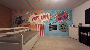 A room with a bed, a wall mural with movie and popcorn themes, a projector, and a clapperboard.