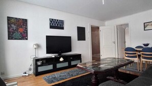 A modern living room with a flat-screen TV, a glass-top dining table, and a seating area with blue chairs. - Hassela Ski Vacation Home in Sweden near the lake and ski slopes (Gävleborgs)