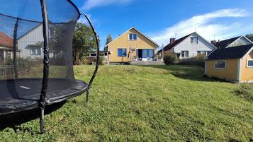 Un trampolín en un jardín con césped y casas al fondo.