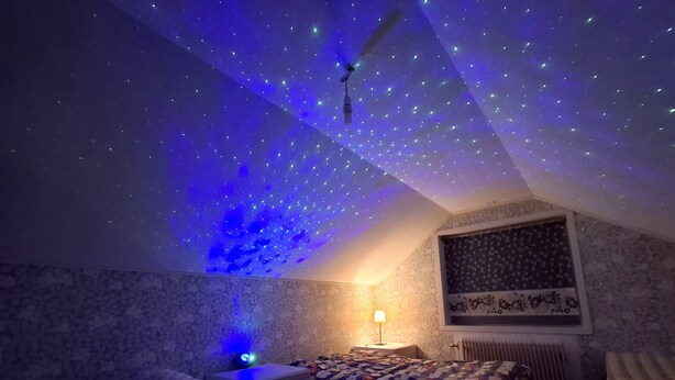 A bedroom with a sloped ceiling, a bed, a nightstand, a lamp, and a window with a patterned curtain. - Hassela Ski Vacation Home in Sweden near the lake and ski slopes (Gävleborgs)