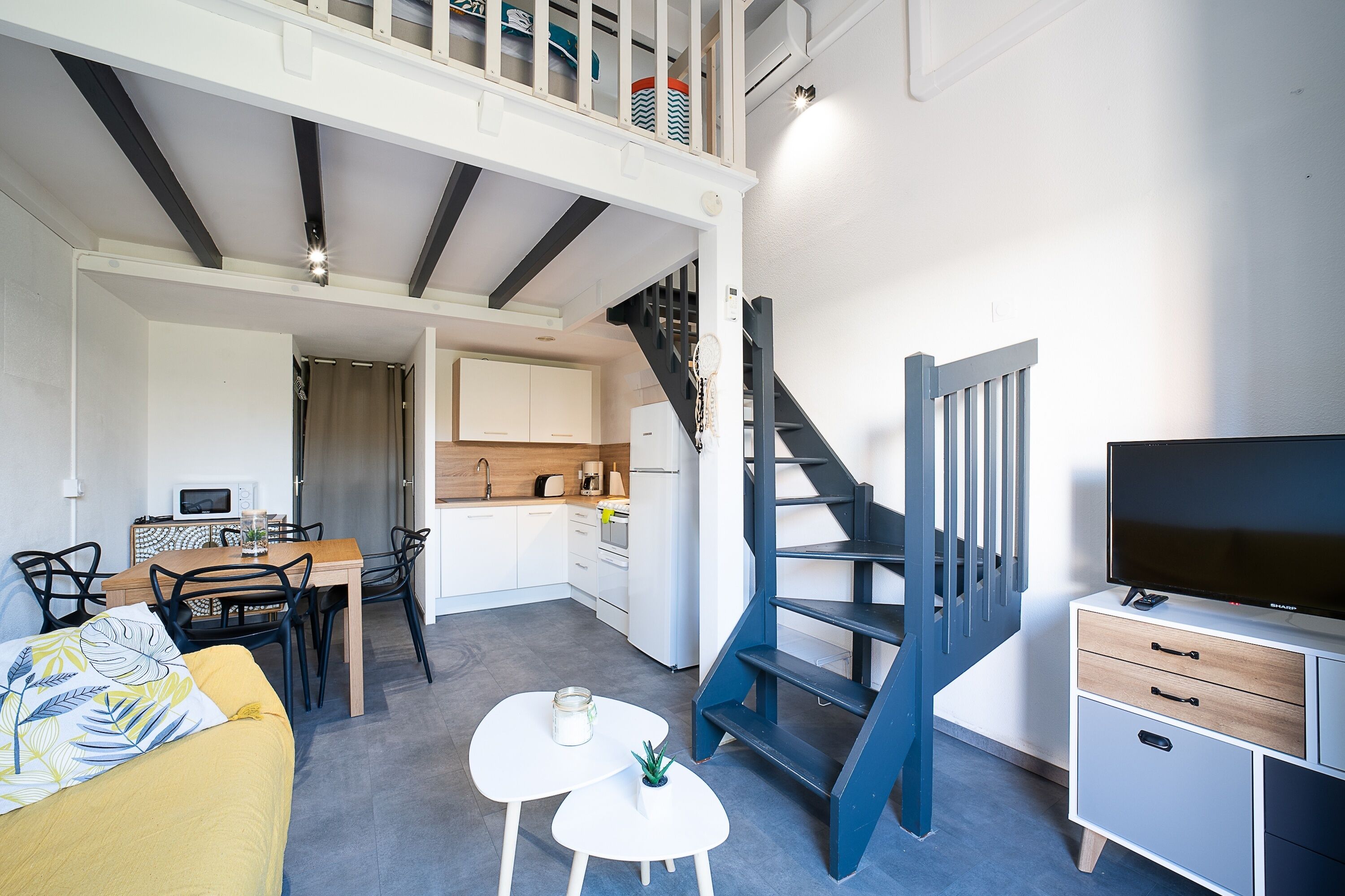 Een modern appartement met een eethoek, keuken, trap en een televisie.