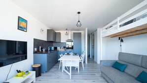 Une cuisine moderne avec un coin repas, un canapé gris et un téléviseur sur le mur de gauche.