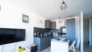 Une cuisine moderne avec des meubles gris, une table à manger blanche et un téléviseur posé sur un meuble blanc.