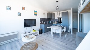 Une cuisine moderne dotée d’un téléviseur à écran plat, de meubles gris et d’un coin repas avec une table et des chaises blanches.