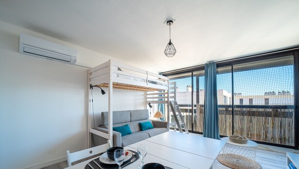 Une chambre moderne avec un lit superposé, une table à manger pour deux personnes et une grande fenêtre donnant sur des immeubles.