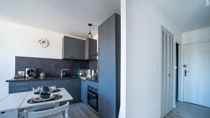 Une cuisine moderne avec des meubles gris, une table à manger pour deux personnes et un petit four.