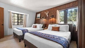 Une chambre avec deux lits, des lambris en bois, une décoration représentant une tête de cerf et une fenêtre avec des rideaux.