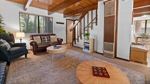 Un salon spacieux avec un canapé en cuir marron, une table basse ronde et un escalier en bois.