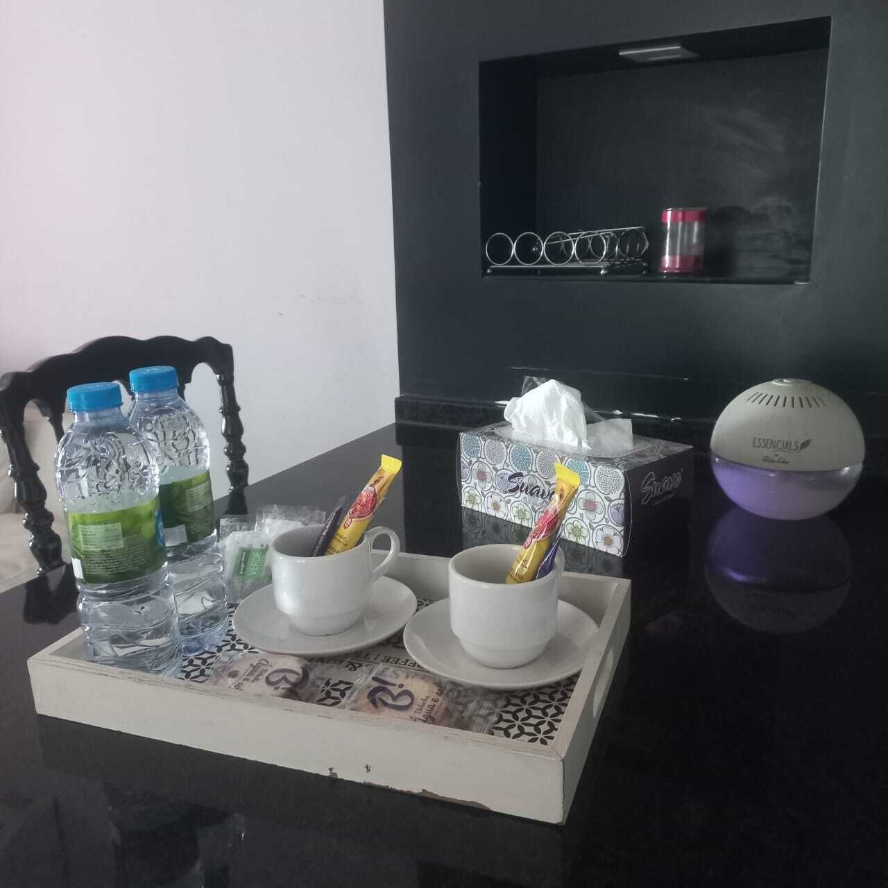 A table with two cups, a tissue box, a humidifier, and bottled water.