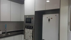 A modern kitchen with white cabinets, a black countertop, a microwave, an oven, and a refrigerator. - Lovely 3-bedroom apartment with AC in vibrant Luanda (Luanda)