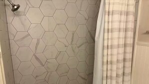 Ein Badezimmer mit sechseckischen Fliesen, einer Dusche inklusive Handbrause und einem gestreiften Duschvorhang.