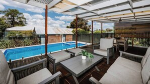 Un espace extérieur abrité comprenant une piscine, des sièges et une vue sur le jardin arrière.