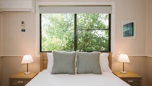 Une chambre avec une grande fenêtre, deux tables de chevet avec des lampes, un lit avec une literie blanche et un climatiseur fixé au mur.
