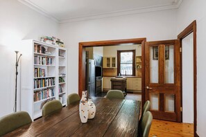 A dining area with a wooden table and chairs, a bookshelf, and a kitchen visible through an open doorway. - Ironbark Oasis Serene Poolside Haven by Mudgee CBD (Mudgee)
