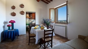 Un comedor con una mesa preparada para dos, vistas al campo a través de una ventana y un techo rústico con vigas a la vista.