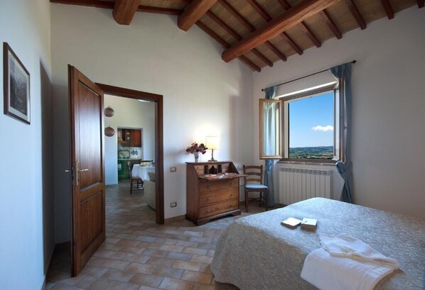 A bedroom with a bed, a dresser, a window with a view, and a door leading to another room. - Agriturismo Fiordaliso (Trevi)