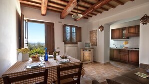 Un comedor con mantel a cuadros, sillas de madera y vistas a través de una ventana abierta.