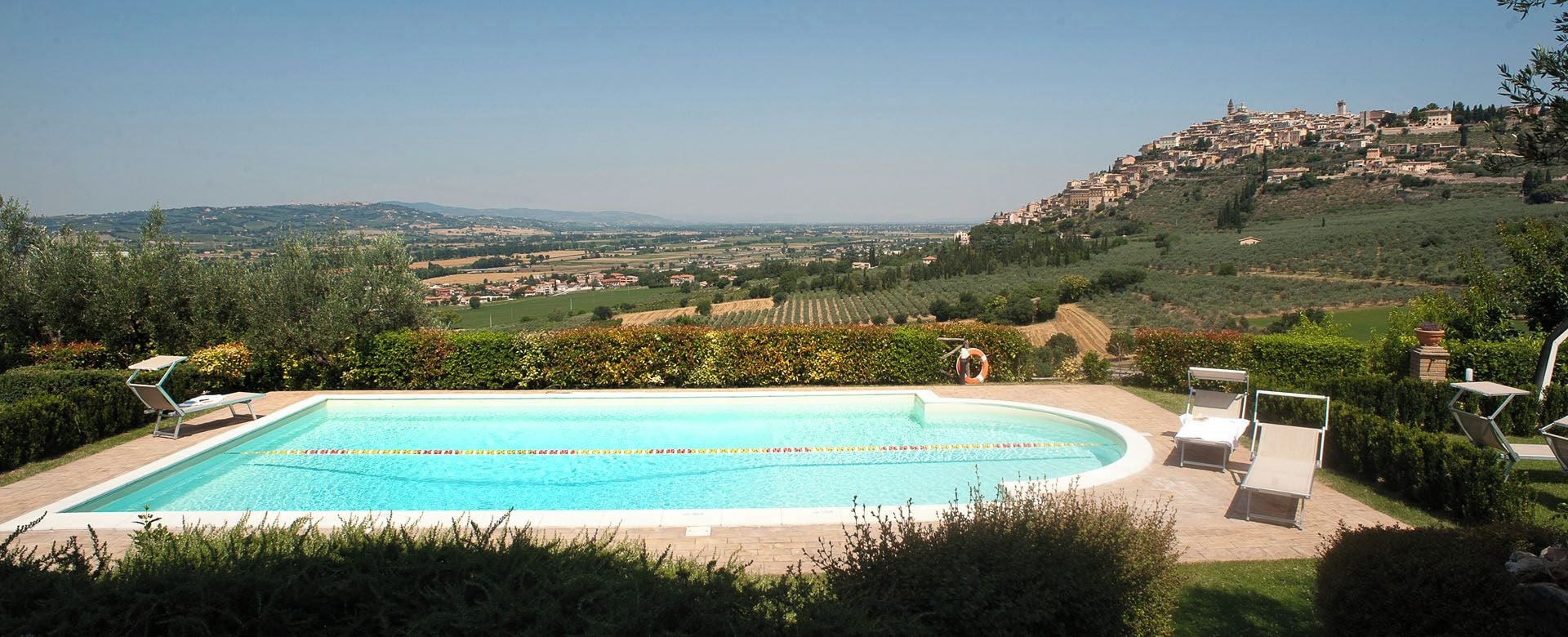 A swimming pool with lounge chairs and a view of a hillside town.