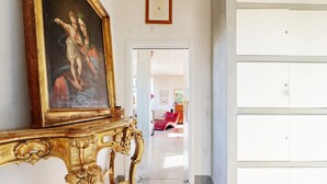 Ein Flur mit einem goldgerahmten Gemälde, einem weißen Schrank und einem roten Sessel im Hintergrund.