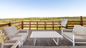 Eine Holzterrasse mit weißen Möbeln, darunter zwei Stühle und ein Tisch, mit Blick auf eine natürliche Landschaft.