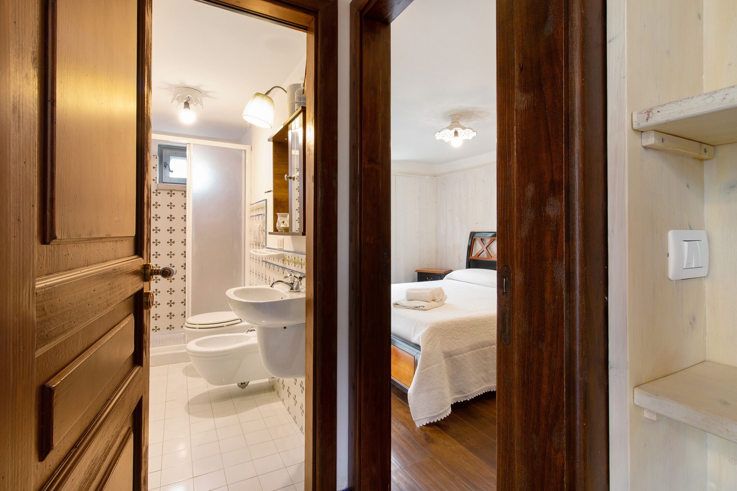 A hotel room with a wooden door, a bathroom with a sink and toilet, and a bed with a white blanket.