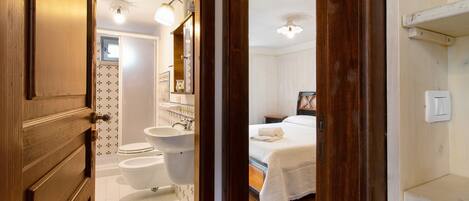 A hotel room with a wooden door, a bathroom with a sink and toilet, and a bed with a white blanket.