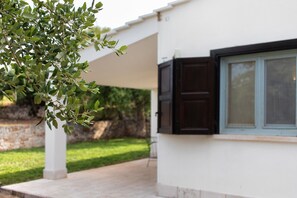A white building with a window and a door, a tree with green leaves, and a stone wall in the background. - Villa 'La Mansarda Di Cecè' with Shared Pool, Wi-Fi and Air Conditioning (Ostuni)