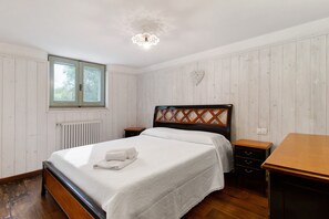 A bedroom with a wooden bed, a nightstand, a dresser, a window, and a radiator. - Villa 'La Mansarda Di Cecè' with Shared Pool, Wi-Fi and Air Conditioning (Ostuni)