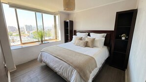 A bedroom with a large window, a bed with white bedding, a wooden floor, and a dark wooden headboard. - Spacious apartment with panoramic view and connectivity in downtown Santiago (San Miguel)