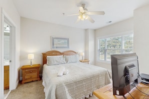 A bedroom with a bed, bedside lamps, a ceiling fan, a window, and a TV on a wooden table. - Golf course view condo with private balcony, W/D, pool & close to beach (Myrtle Beach)
