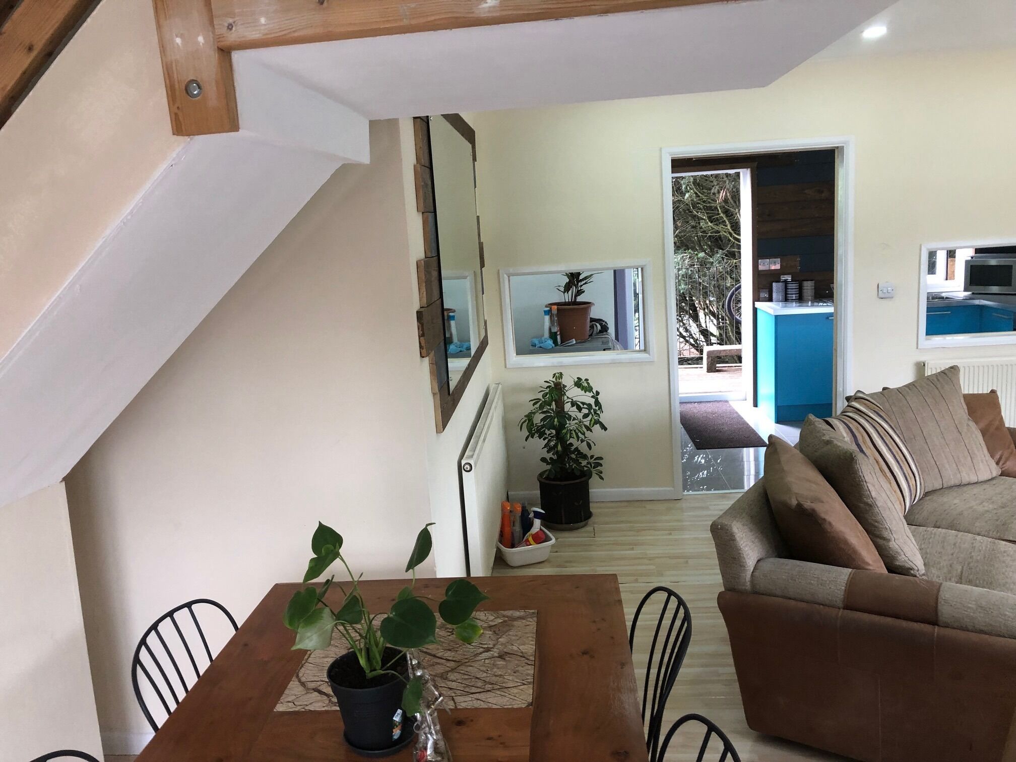 A cozy living room with a wooden dining table, a sofa, and a staircase leading to an upper level.