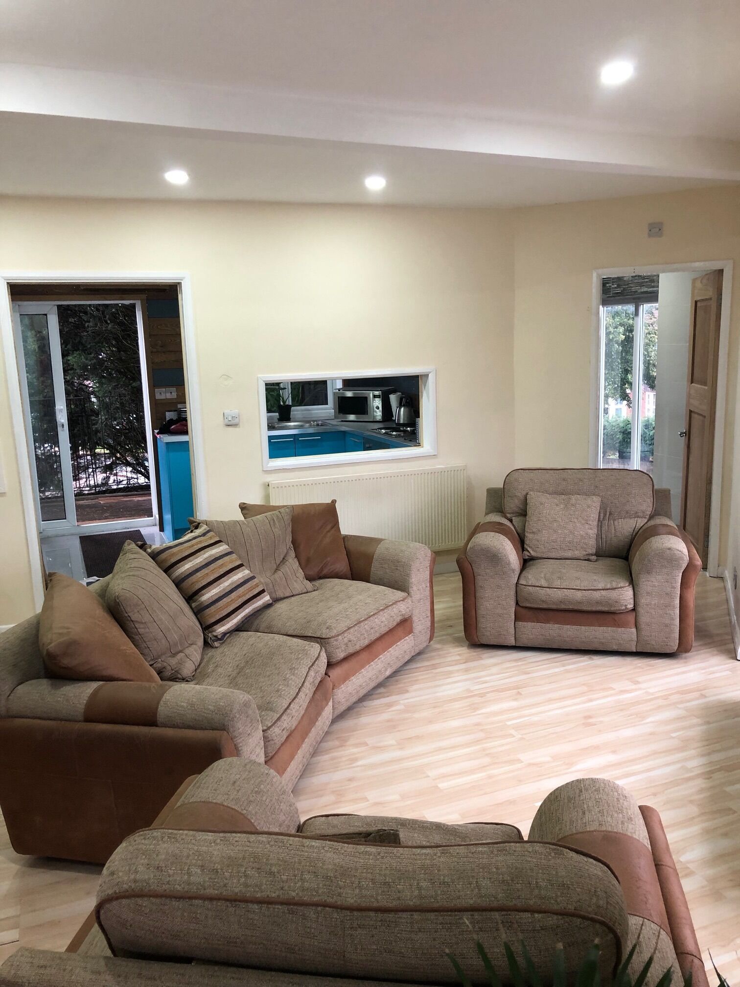 A living room with a sectional sofa, a recliner, and a built-in kitchen area with a microwave and kettle.