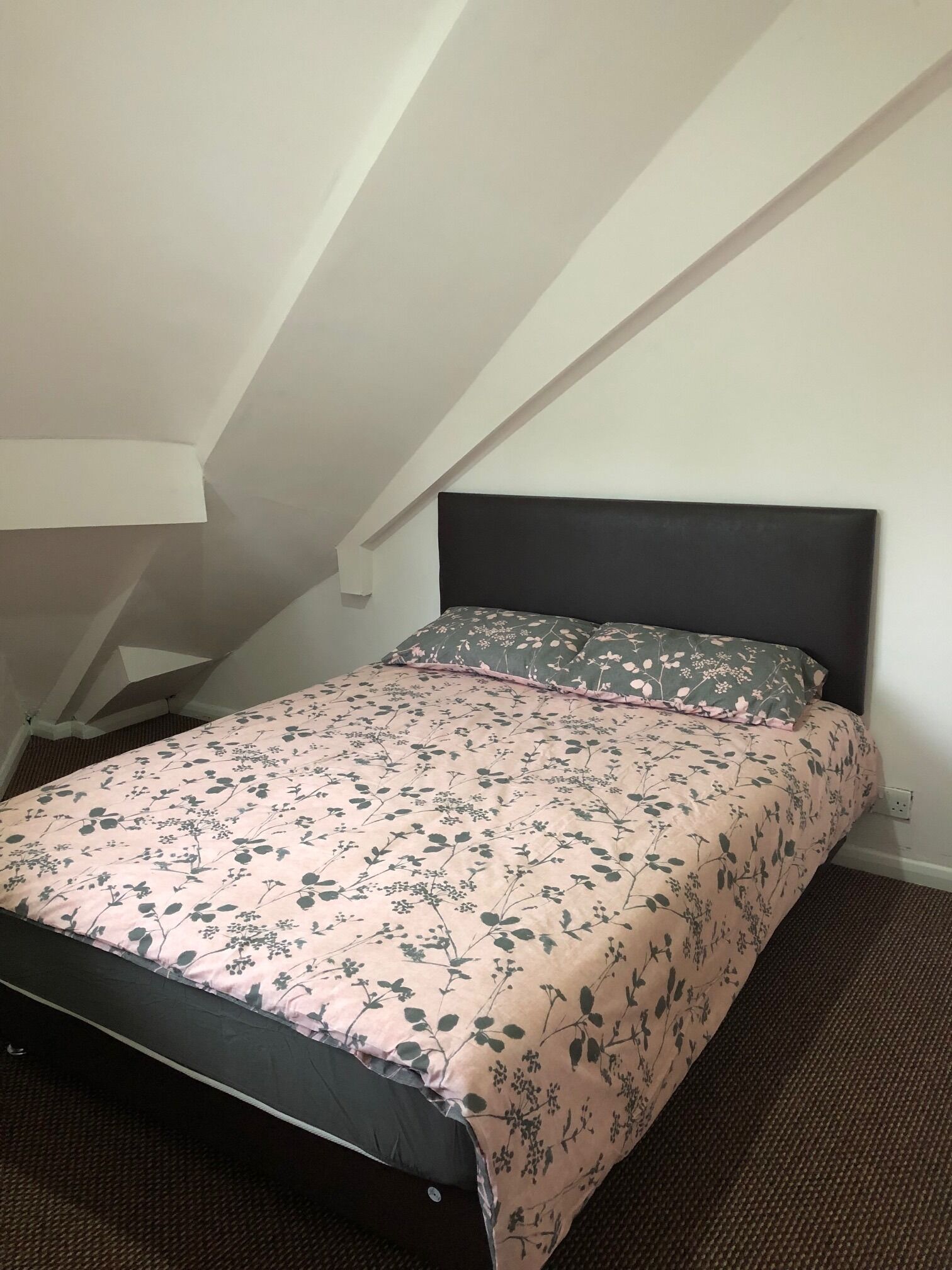 A bedroom with a bed, a sloped ceiling, and a plain wall.