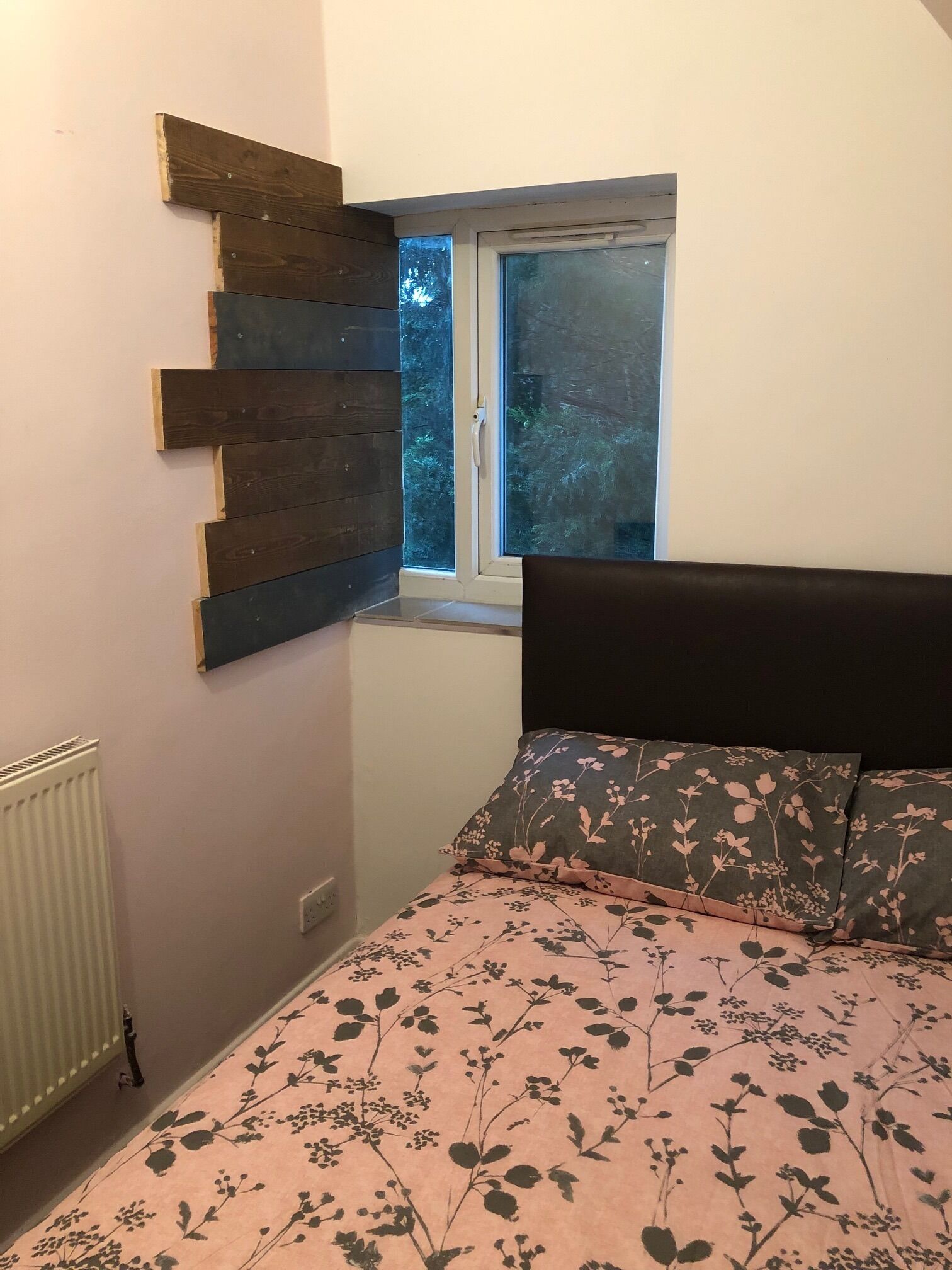 Une chambre à coucher comprenant un lit, une fenêtre, un radiateur et un panneau en bois fixé au mur.