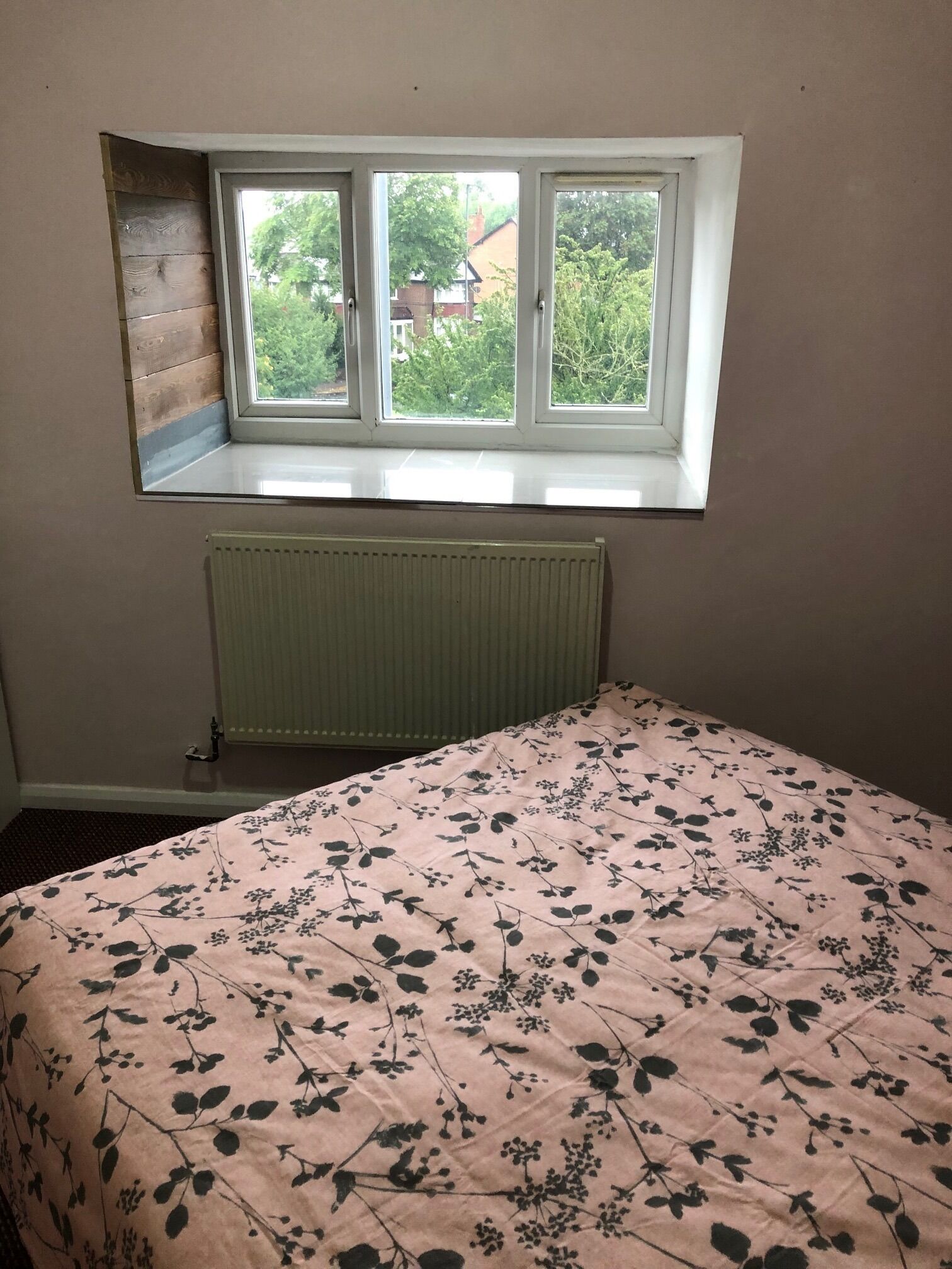 A bedroom with a window, a radiator, and a floral bedspread.