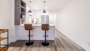 A modern kitchen with two bar stools, a built-in island, and pendant lighting. - Cozy&Modern New 1 Bedroom Condo (Surrey)