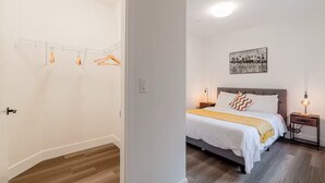 A bedroom with a bed, bedside tables, a hanging light fixture, and a wall-mounted picture. - Cozy&Modern New 1 Bedroom Condo (Surrey)