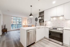 Una cocina moderna con armarios blancos, un lavavajillas de acero inoxidable, un horno empotrado y un amplio ventanal con vistas a la ciudad.