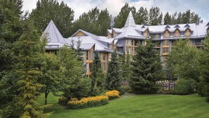 Un grande edificio a più piani con una facciata simmetrica, circondato da vegetazione lussureggiante e un prato curato.