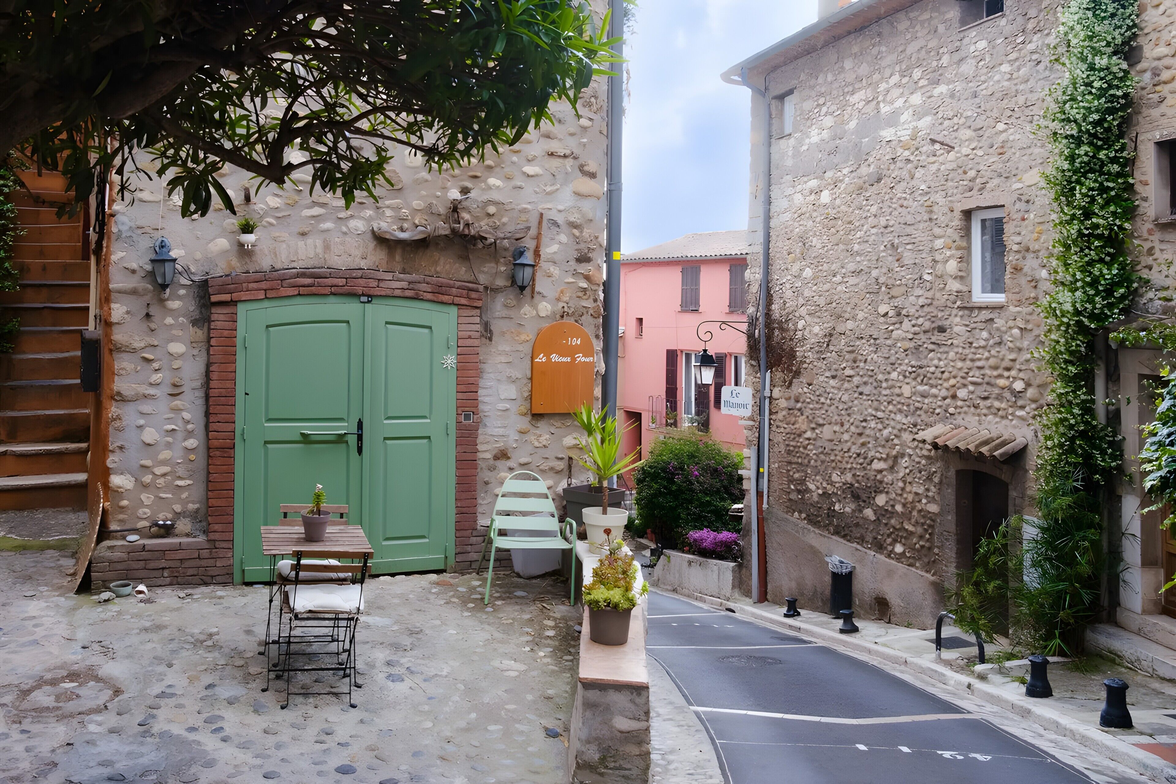 Un vicolo stretto con un edificio in pietra, una porta verde, una panchina e un tavolo con una pianta in vaso.