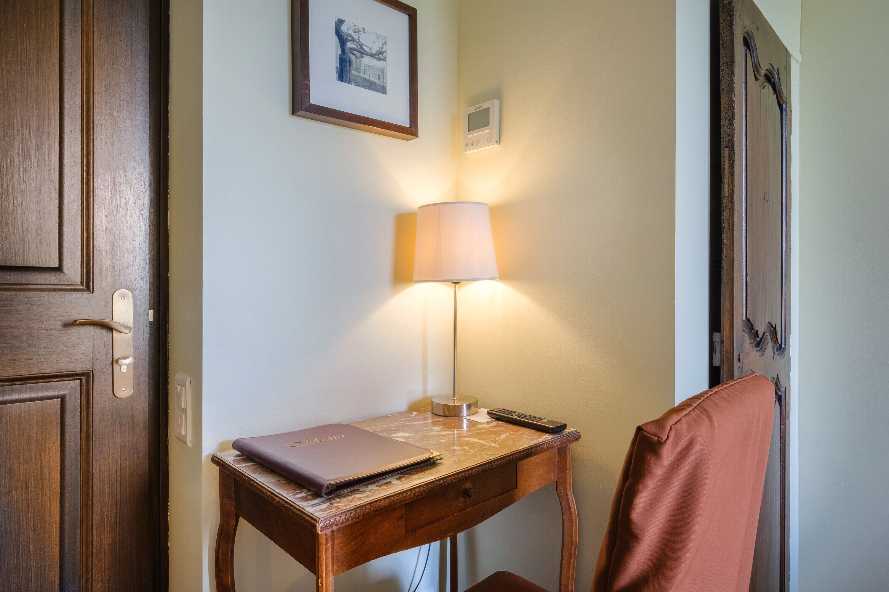 Un bureau en bois avec une lampe, une télécommande et un classeur.