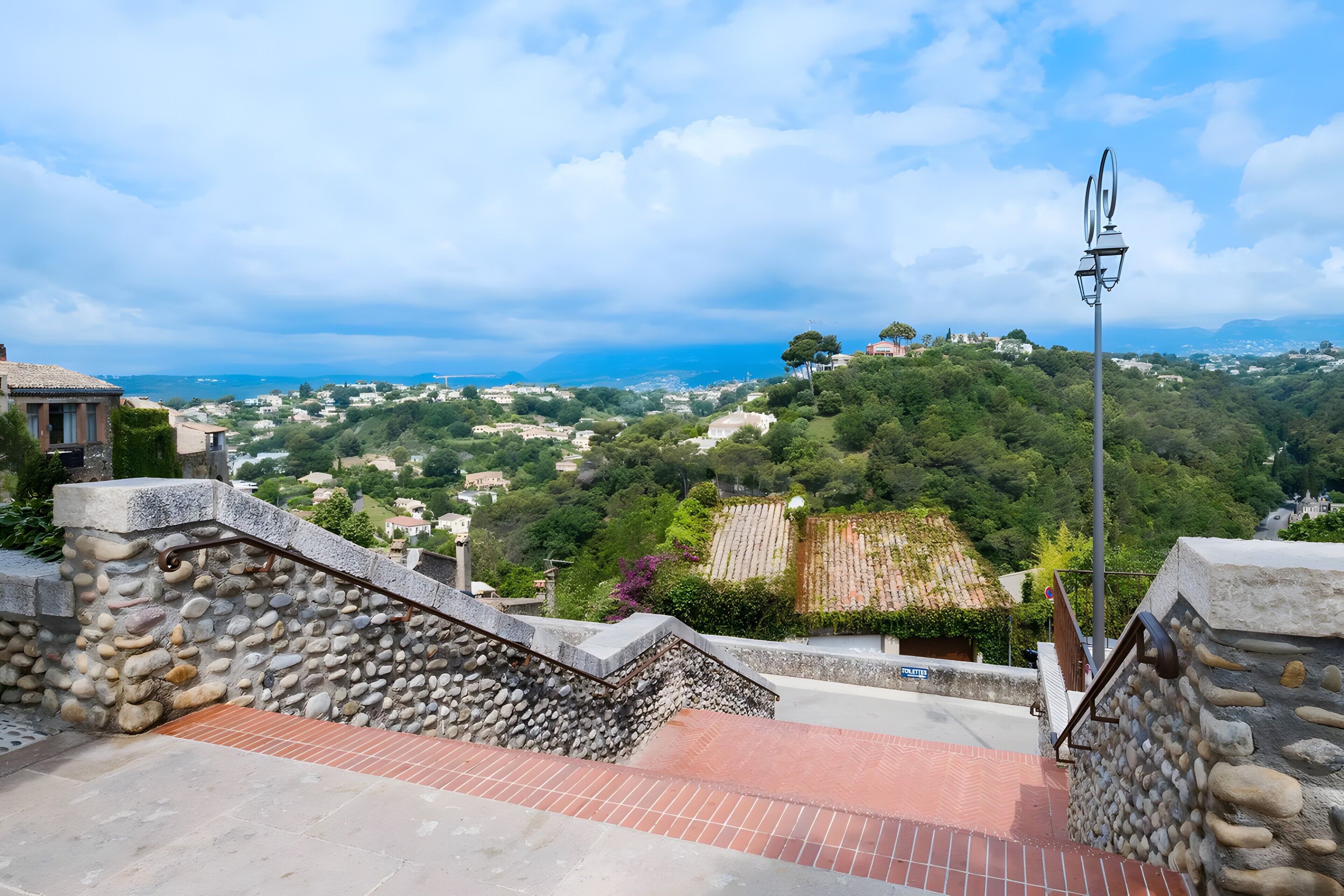 Eine Steintreppe führt zu einer Terrasse mit Blick auf eine Küstenstadt.